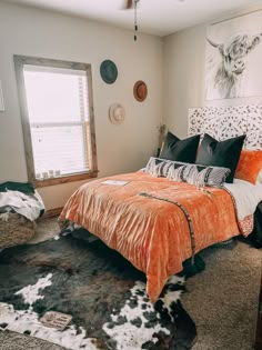 a bedroom with an orange bed spread and cow hide rug