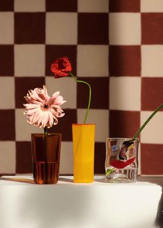 three vases with flowers in them sitting on a table next to a checkered wall