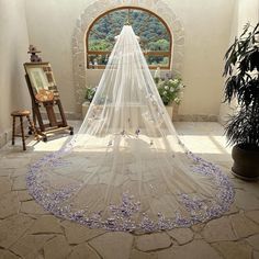 a white wedding veil with purple flowers on the bottom is in front of a window