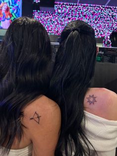 two women with tattoos on their backs sitting in front of a television screen at night