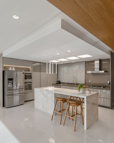 a kitchen with marble counter tops and stools in front of an island that's surrounded by stainless steel appliances