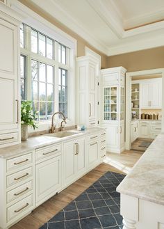 a large kitchen with white cabinets and marble counter tops, along with a blue rug on the floor