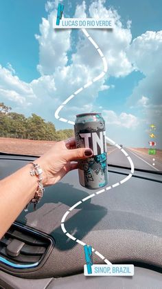 a person is holding up a can of beer in their hand while driving down the road