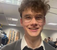 a young man wearing glasses and a bow tie smiles at the camera while standing in an office