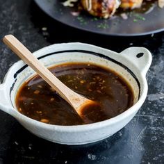 a white bowl filled with sauce next to a plate of food on a black table