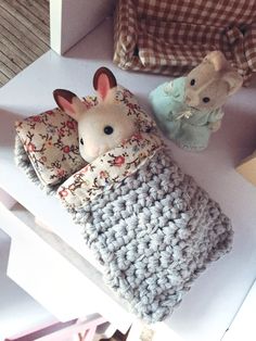 two stuffed animals sitting on top of a white table next to some blankets and pillows