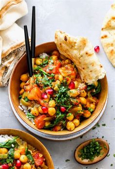 two bowls filled with food next to pita bread on top of a white table