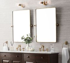 two mirrors are above the double sink vanity in this bathroom with white towels and gold fixtures