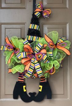 a halloween wreath hanging on the front door decorated with colorful ribbons and black booties