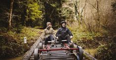 two people sitting on top of a train track in the middle of some trees and bushes