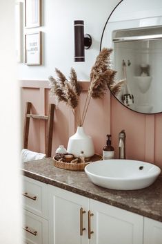 a white sink sitting next to a mirror on top of a bathroom counter under a round mirror