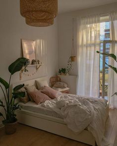 a bedroom with white walls and wooden flooring, plants on the side of the bed