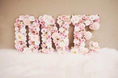 the word mom spelled with pink and white flowers on top of a fur rug in front of a wall