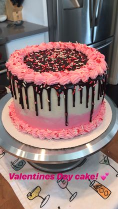 a pink and white cake with chocolate drips on it sitting on top of a table