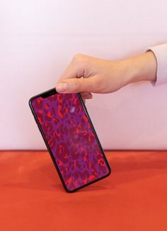 a hand holding an iphone in front of a pink wall with red and purple designs