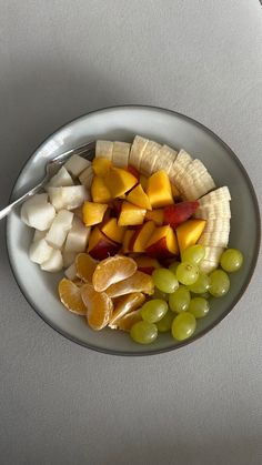 a white plate topped with fruit and cheese on top of a gray countertop next to a silver spoon