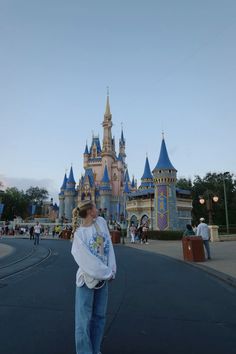 a woman standing in front of a castle at disneyland world with her arms around her face