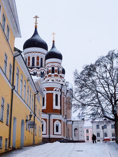 an old church with two towers in the middle of a snow covered street next to tall buildings