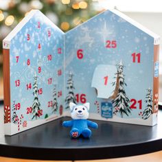 a small blue teddy bear sitting in front of a house shaped like a christmas tree