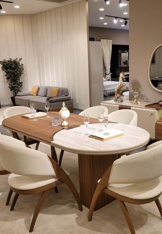 a dining room table with white chairs and a round mirror on the wall above it