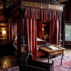 a bed with red curtains and a desk in front of it on top of a rug