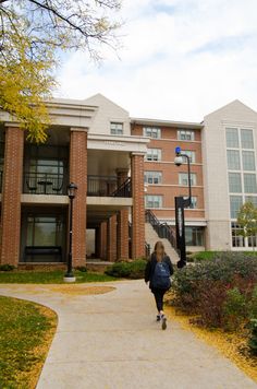 a woman walking down a sidewalk in front of a brick building with balconies