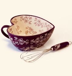 a purple and white bowl with whisk in it next to an egg beater