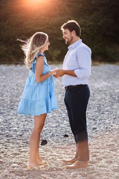 a man and woman standing next to each other on a beach at sunset with the sun behind them