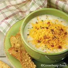 a bowl of soup with cheese and crackers on a green plate next to a piece of bread