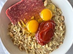 two eggs on top of oatmeal with ketchup in a bowl