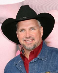 a man wearing a cowboy hat standing in front of a pink wall and smiling at the camera