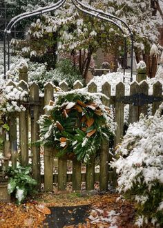 a wooden fence with a wreath on it in the snow next to trees and bushes