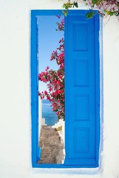 an open window with blue shutters and pink flowers on the outside, looking out to sea