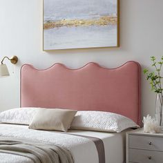 a bed with a gray headboard and white sheets in a small room next to a painting on the wall