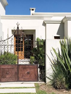 an iron gate with wooden doors in front of a white house and cactus plants on the sidewalk