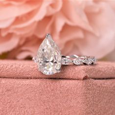 a diamond ring sitting on top of a pink box with flowers in the back ground