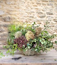 a vase filled with flowers sitting on top of a wooden table next to a stone wall