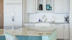 a kitchen with white cabinets and marble counter tops