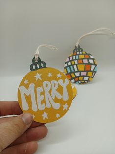 someone is holding two ornaments with merry written on one ornament and the other has a string attached to it