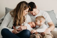 a man and woman holding a baby while sitting on a bed with their arms around each other