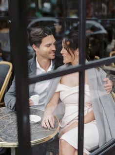 a man and woman are sitting at an outdoor table looking into each other's eyes