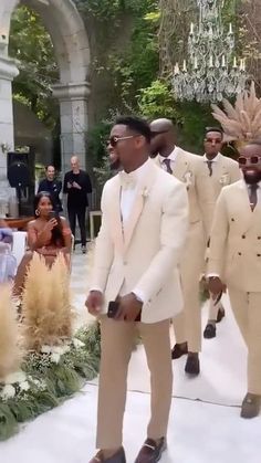 two men in white suits walking down the aisle with other people watching them from behind