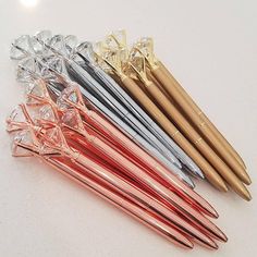 five different colored pens sitting next to each other on a white surface with gold and silver tips