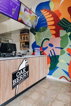 the interior of a restaurant with colorful murals on the wall and counter top, along with televisions above it