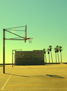 an empty basketball court with palm trees in the background