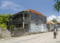 a woman walking down the street in front of an old wooden house with rusted roof