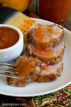 two pieces of meat on a plate next to a bowl of sauce and a fork