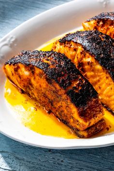 three pieces of grilled salmon on a white plate with yellow sauce in the middle