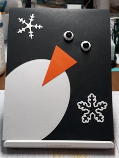 a snowman made out of black paper with white and orange decorations on it's face