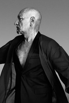 a bald man in a black shirt and blazer with his hands on his hips